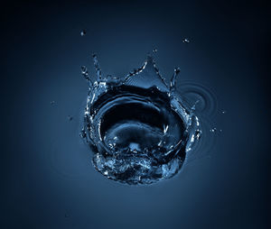 Close-up of drop splashing on water against black background