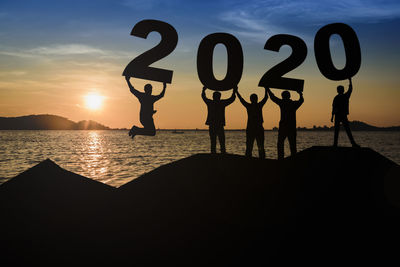 Silhouette people standing by sea against sky during sunset