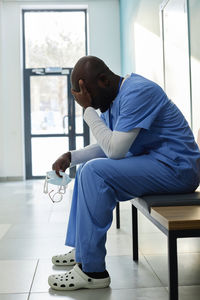 Tired doctor with head in hand sitting on bench in hospital corridor