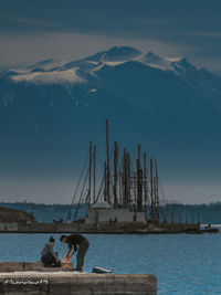 People sitting on pier over sea against sky