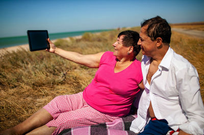  elderly couple sitting on beach using tablet video call