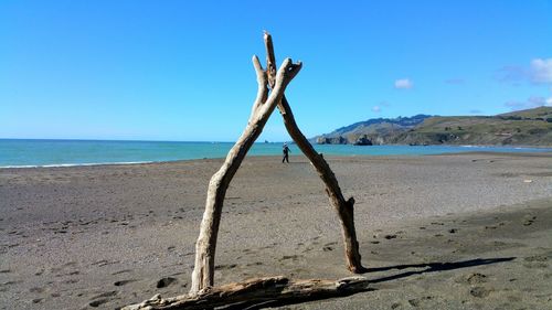 Scenic view of driftwood log arch in beach by sea against clear blue sky