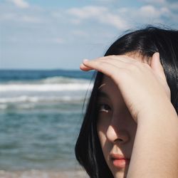 Close-up portrait of woman shielding eyes while standing at beach