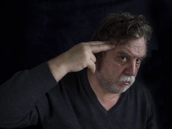 Portrait of mature man shooting himself against black background