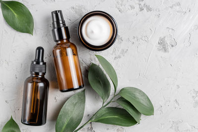 A set of cosmetic products in dark glass on a concrete background with green leaves natural organic 