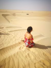 Rear view of woman sitting on sand at beach desertloveinfinity