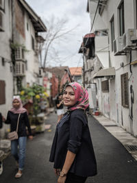 Portrait of young woman standing on road amidst buildings