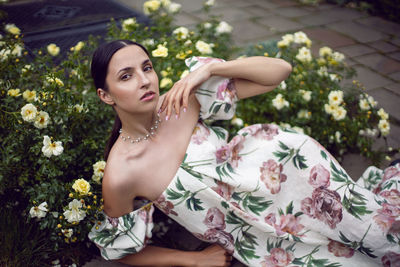 Outdoor portrait of a beautiful girl in a dress lying on the ground next to a white roses