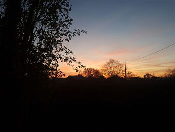 Silhouette trees on landscape against sky at sunset