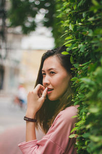 Smiling woman looking away while standing against plants