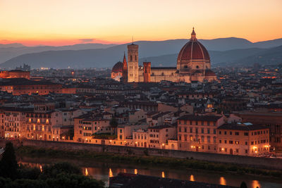 Illuminated buildings in city against sky during sunset