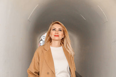 Elegant blonde lady walks confidently through a city tunnel, dressed in a fashionable coat