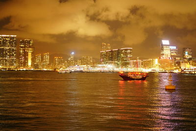 Illuminated buildings by river against sky at night