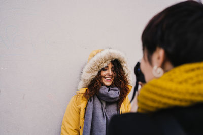 Woman photographing smiling friend against wall