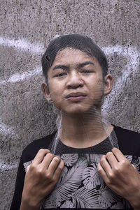 Portrait of boy wearing net while standing against wall