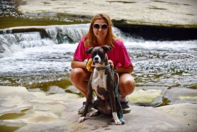 Portrait of smiling young woman with dog at riverbank