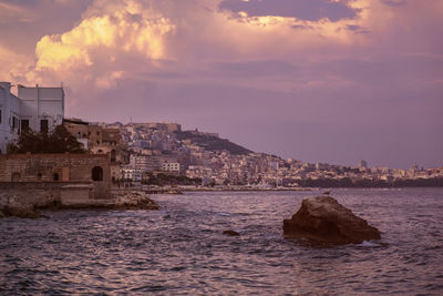 Sea by buildings against sky during sunset