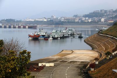 Boats in river by cityscape against sky