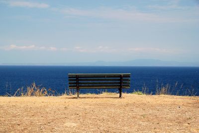 Empty bench at beach against sky