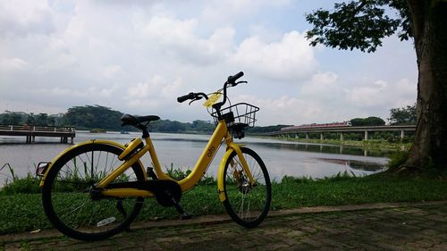 Yellow bicycle parked on roadside by lake against sky