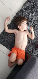 High angle view of shirtless boy looking away while lying on rug at home