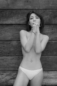 Portrait of shirtless young woman standing against wooden wall