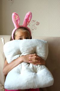 Portrait of girl covering face with cushion at home