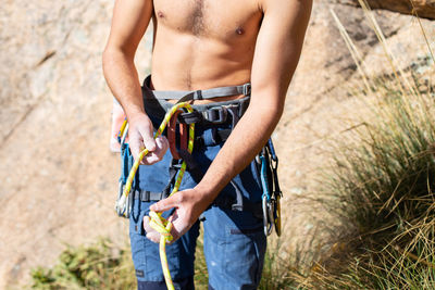 Midsection of shirtless man wearing safety harness while standing outdoors