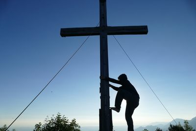 Side view of silhouette man climbing on electricity pylon