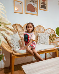 Happy little girl sitting on the rattan couch in a boho interior design.