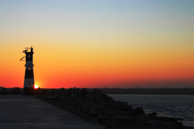 Lighthouse by sea against romantic sky during sunset