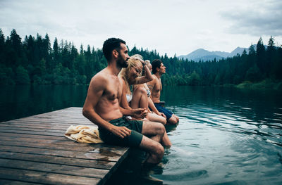 Young man sitting on lake against sky