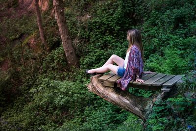 Rear view of man sitting on tree stump in forest