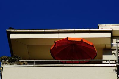 Low angle view of balcony with red umbrella against blue sky