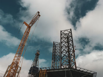 Low angle view of cranes at construction site against sky