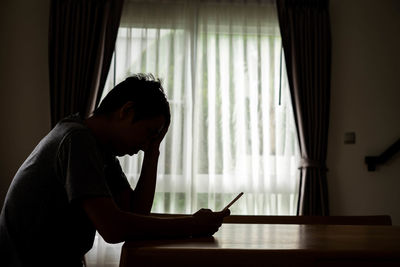 Side view of young man using mobile phone at home