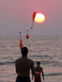 Rear view of men at beach against sky during sunset