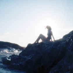 Side view of a silhouette woman sitting on beach