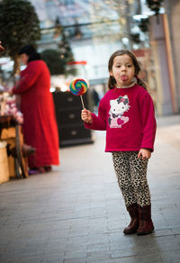 Portrait of girl eating lollipop while standing on footpath in city