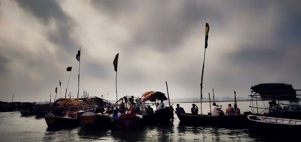 People on boats in sea against cloudy sky