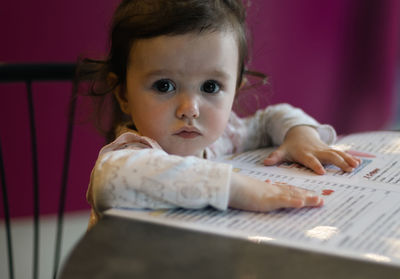 Portrait of a caucasian baby girl with a menu in a cafe.