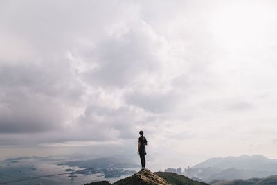 Woman standing on mountain against cloudy sky