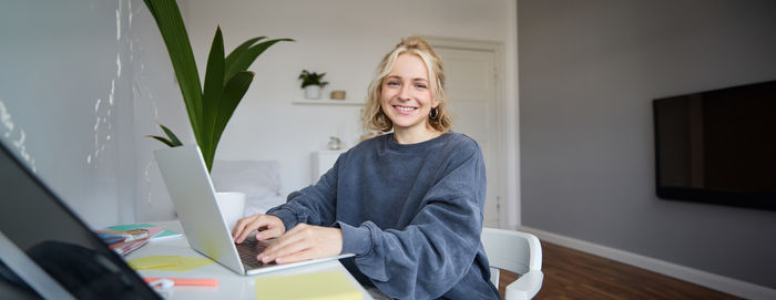 Portrait of young woman using laptop while sitting on table at home
