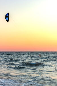 Man parasailing over sea against sky during sunset