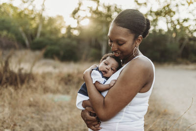 Portrait of young mother holdiing infant daughter in backlt field