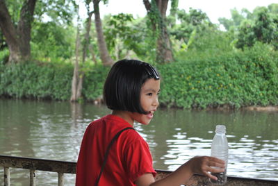Girl holding bottle while standing against lake