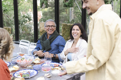 Cheerful family listening to young man talking during dinner party