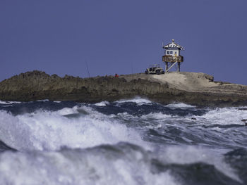 Lighthouse by sea against clear sky