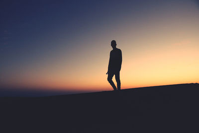 Silhouette man standing on street against sky during sunset