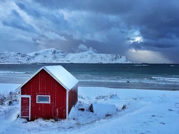 Barn on snow covered beach against cloudy sky